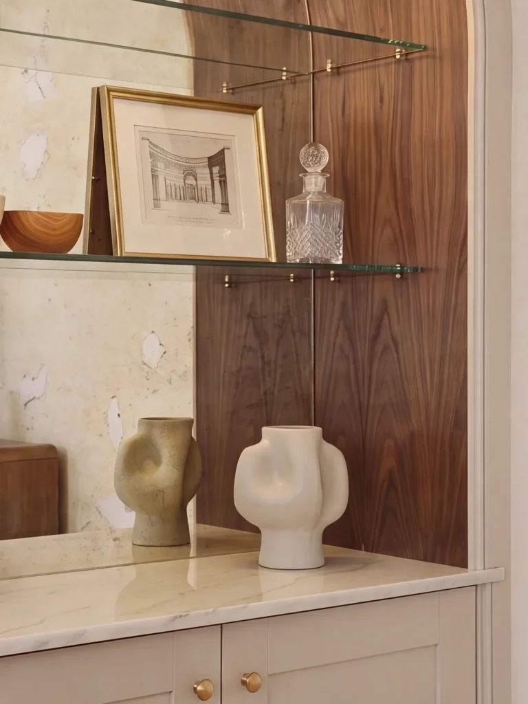 Glass shelf with a framed print and decanter in front of walnut panelling over a cream cabinet