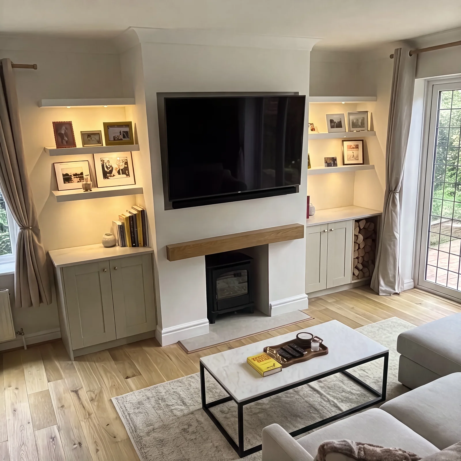Cream fireplace media wall with lit floating alcove shelves, an oak mantel and a wall-mounted TV