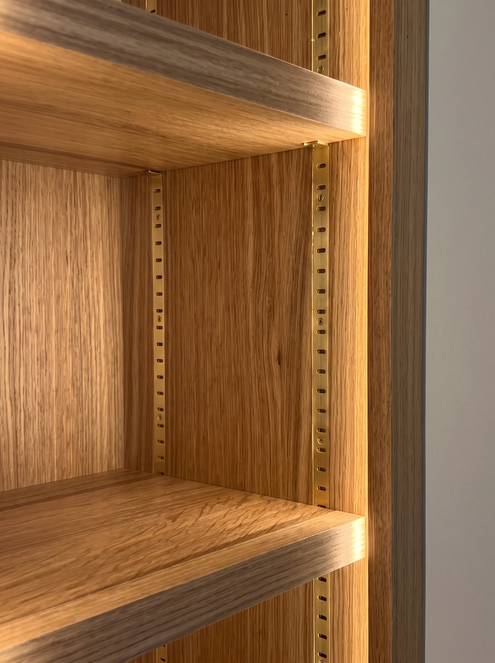 Close-up of lit oak shelves with an adjustable shelf strip inside an alcove