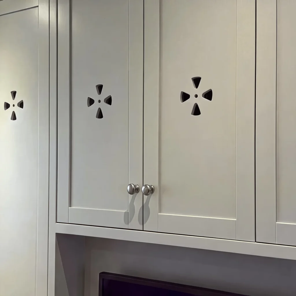 Close-up of pale grey shaker doors with decorative cut-out vents and chrome knobs