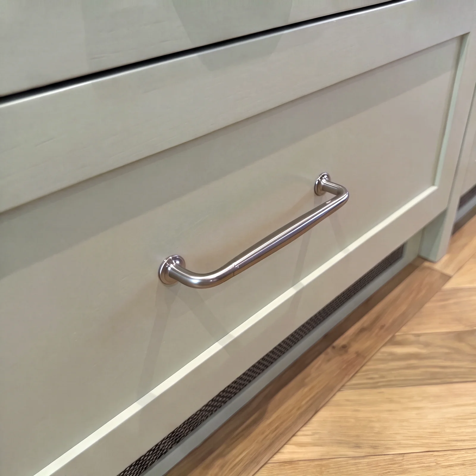 Close-up of a pale grey shaker drawer with a chrome bar handle above a herringbone floor