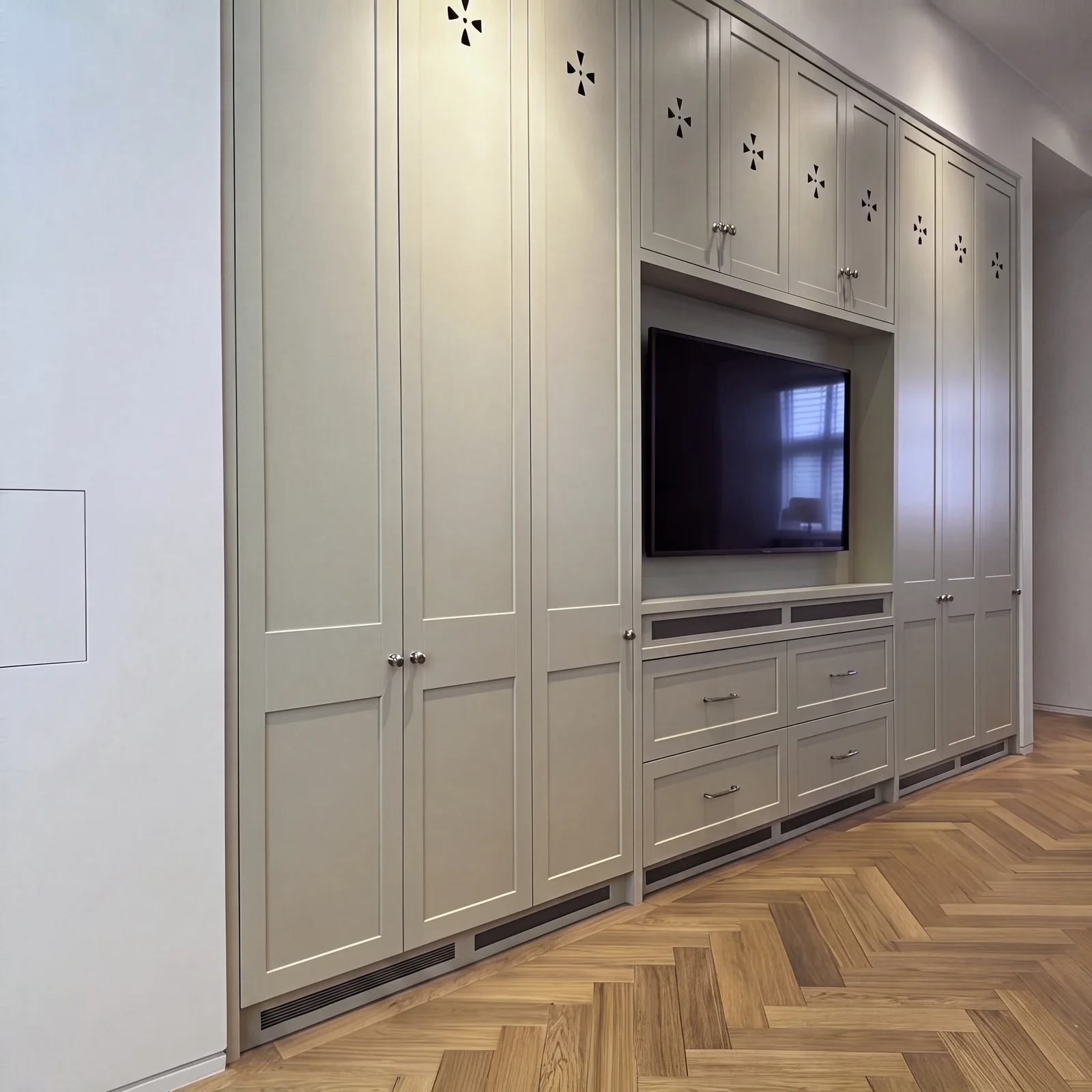 Long pale grey built-in media wall with full-height cupboards on a herringbone oak floor