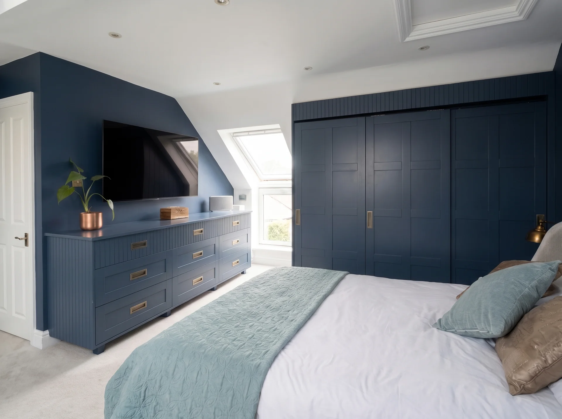 Loft wardrobes in Fulham: loft bedroom with navy fitted wardrobes and a navy chest of drawers below a TV