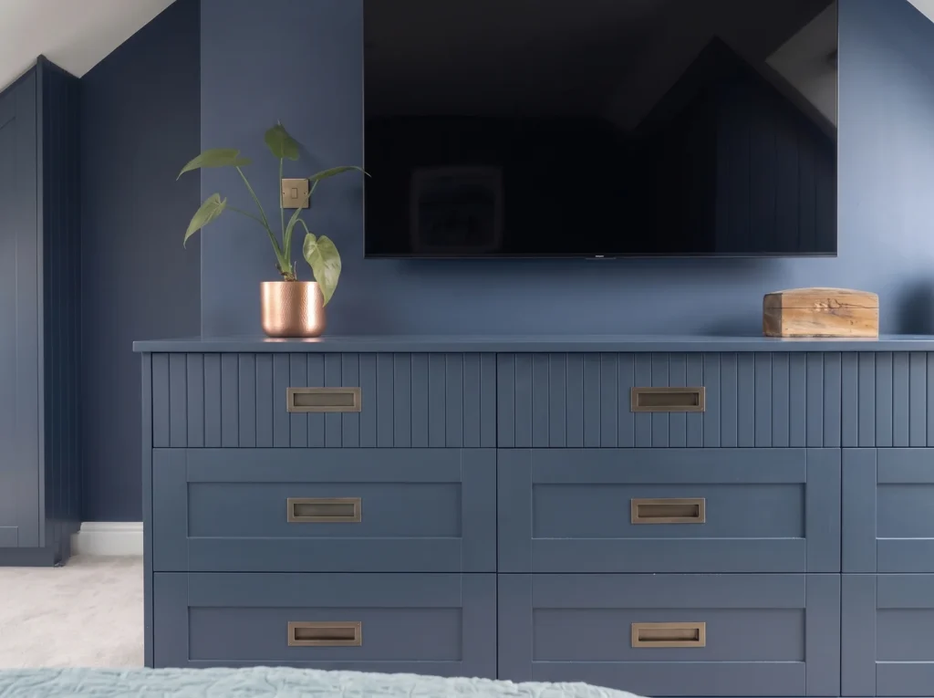 Navy reeded chest of drawers with brass handles below a wall-mounted TV