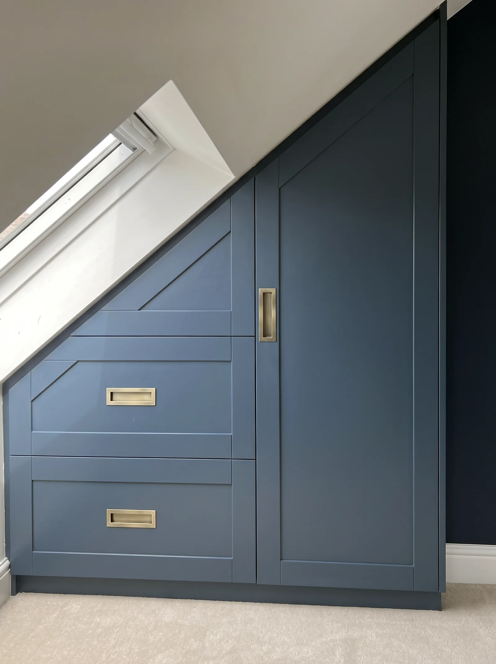 Navy shaker eaves cupboard with brass-handled drawers beneath a sloping roof window