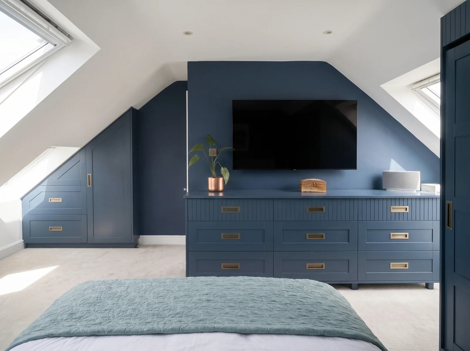 Loft bedroom with a navy eaves cupboard and navy drawers below a TV between two roof windows