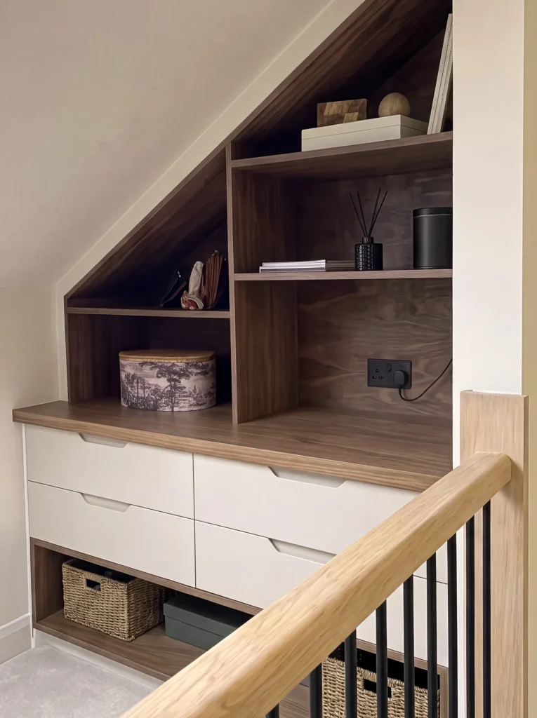 Angled walnut eaves shelving above cream drawers and a basket shelf by the banister