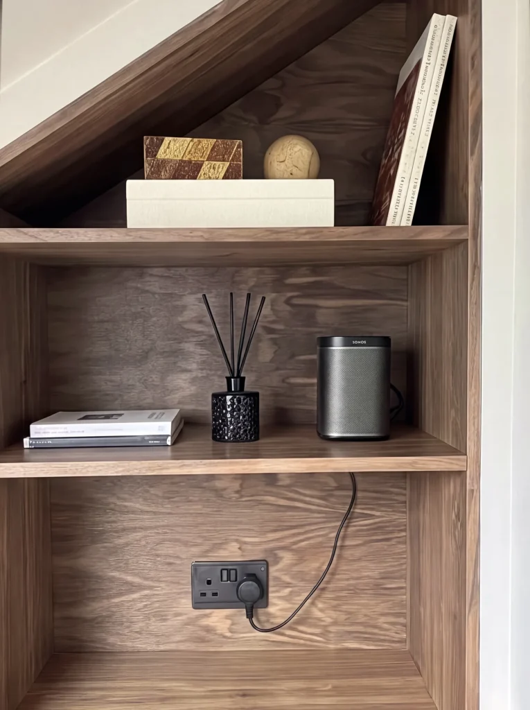 Walnut shelves with a diffuser, speaker and books above a built-in socket