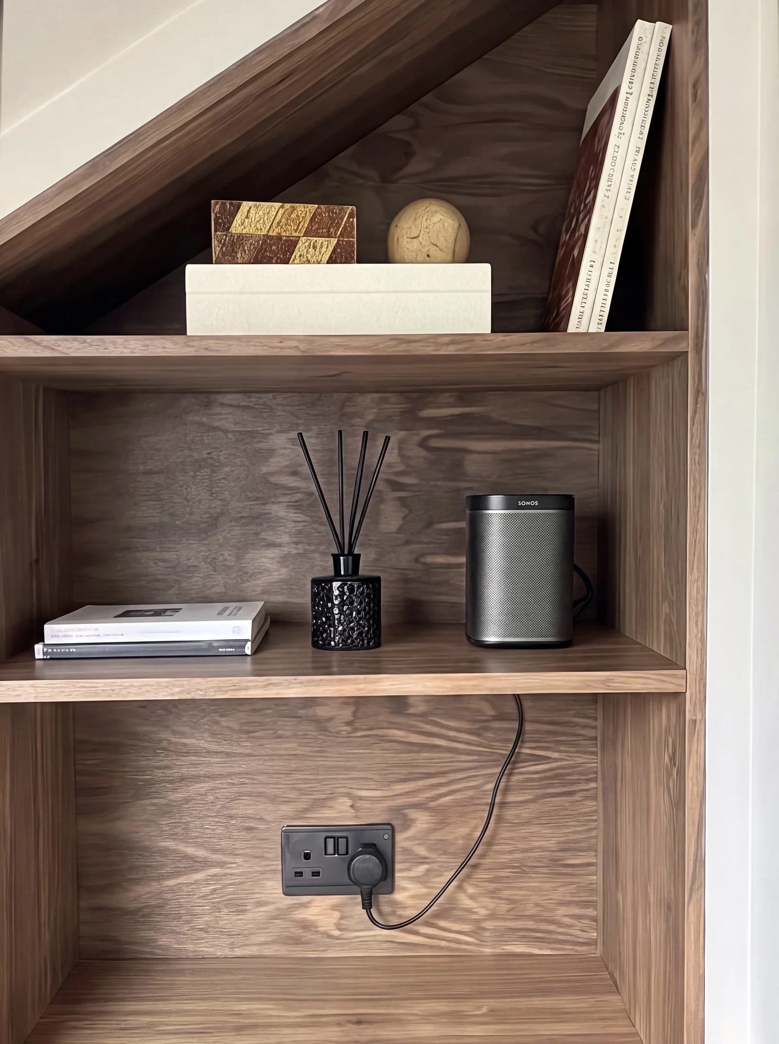 Walnut shelves with a diffuser, speaker and books above a built-in socket