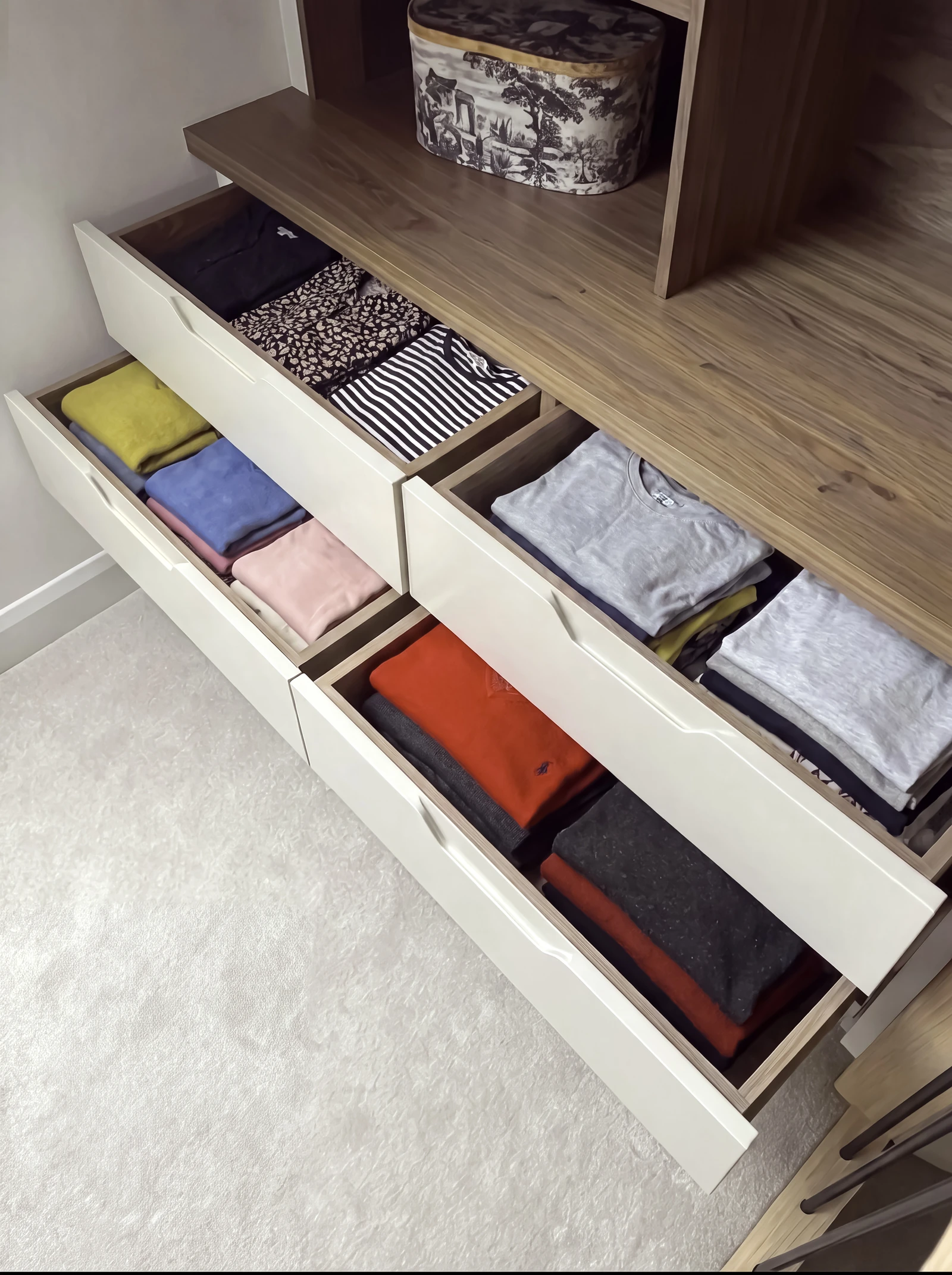 Open cream drawers with folded T-shirts beneath a walnut shelf