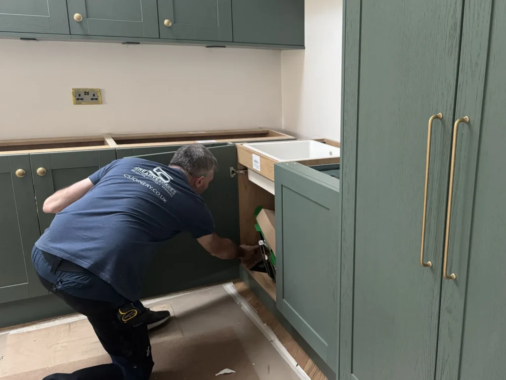 Joiner fitting green shaker kitchen cabinets with brass bar handles