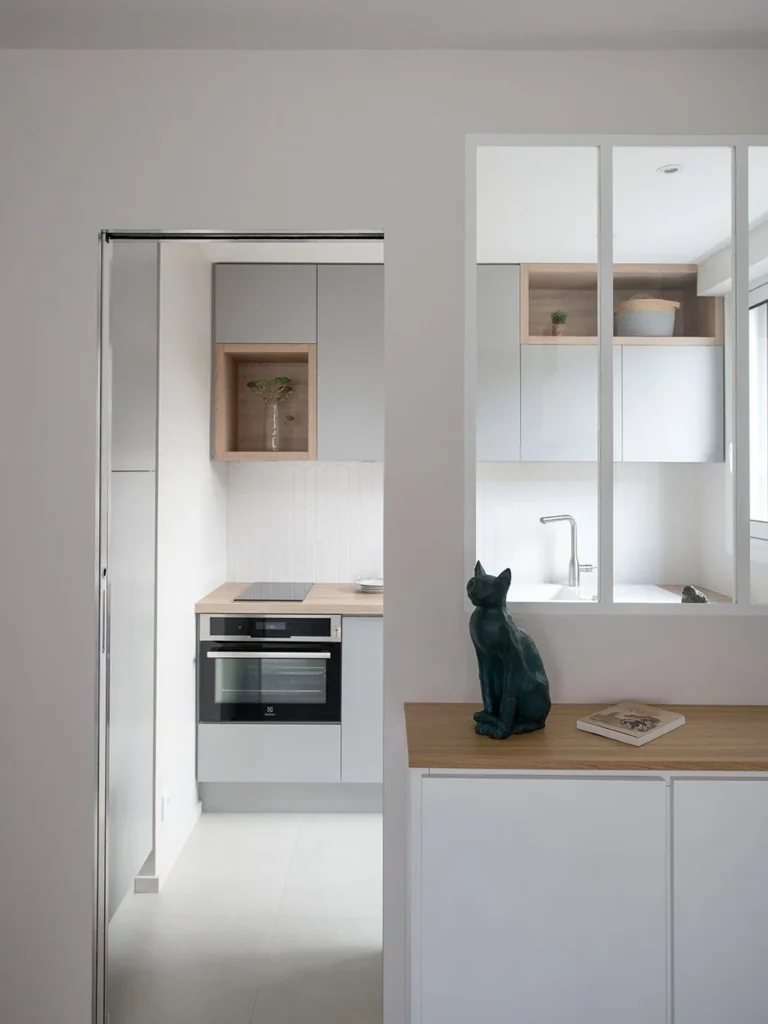 View through a doorway to a grey kitchen with an internal glazed window and an oak-topped cabinet