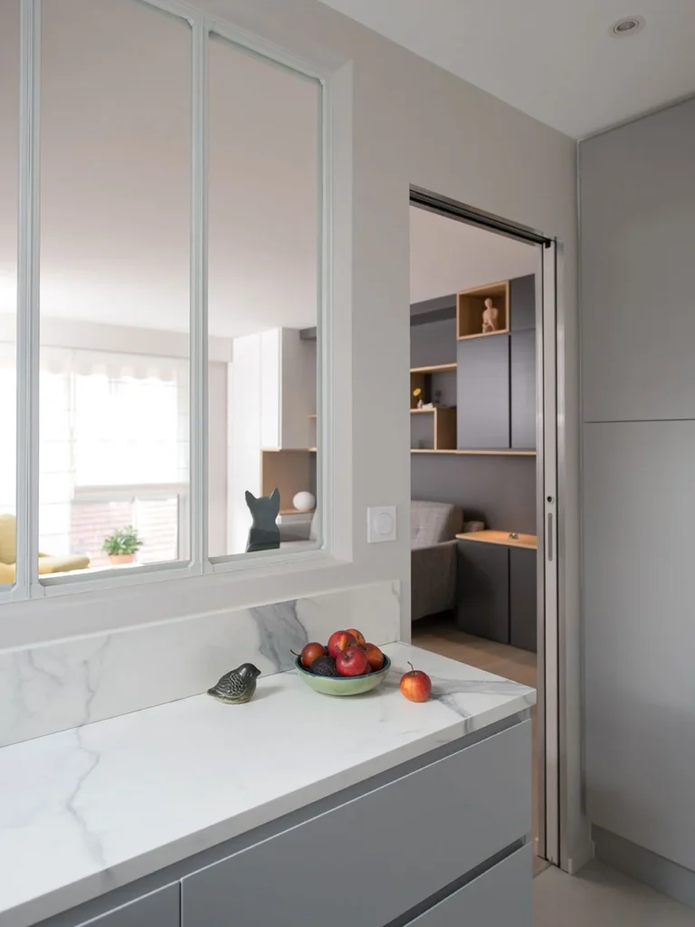 Grey galley kitchen with a white marble-effect worktop beneath an internal window