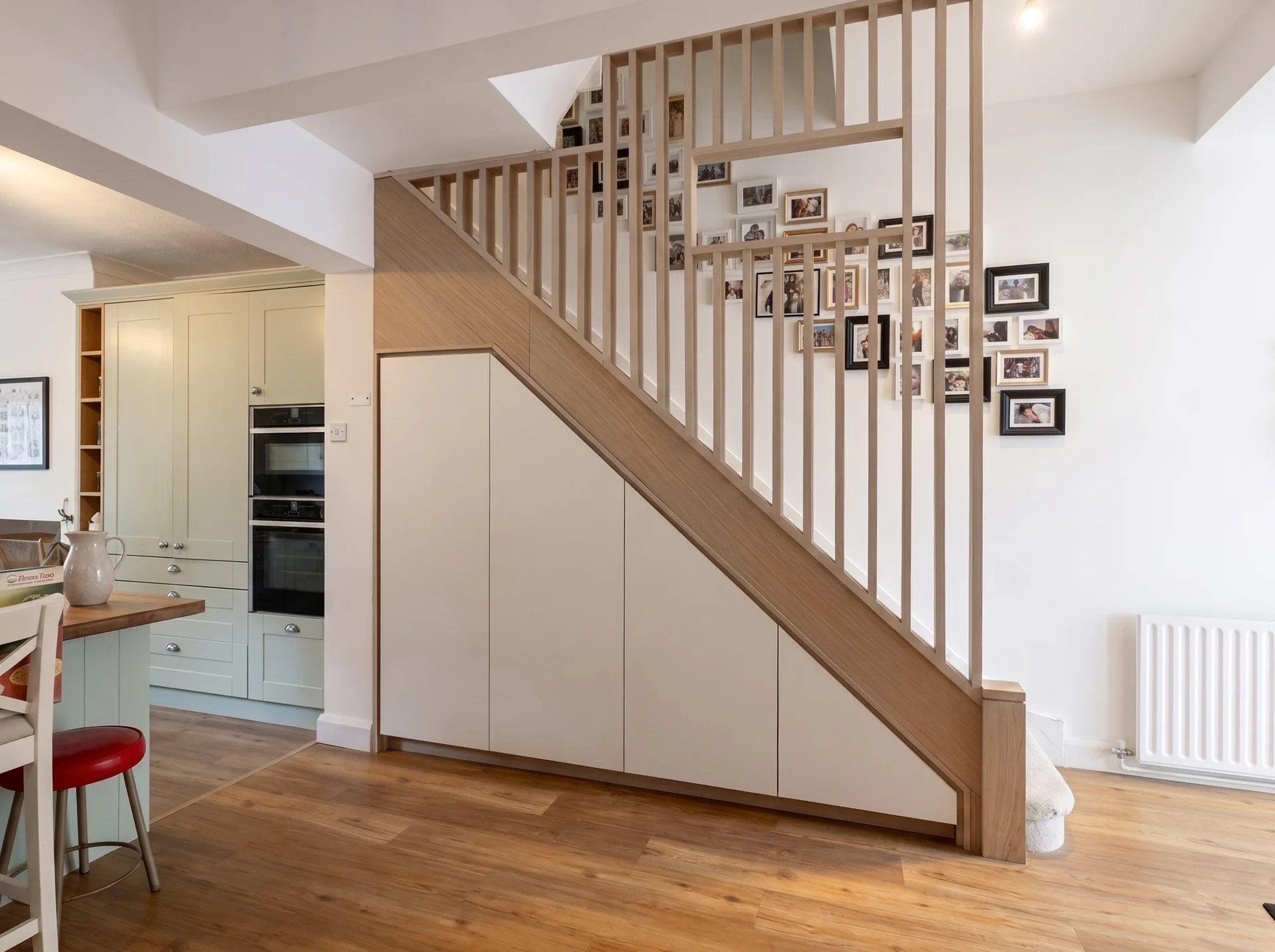 Understairs storage in Bromley: white handleless understairs cupboards beneath an oak staircase with a slatted oak balustrade