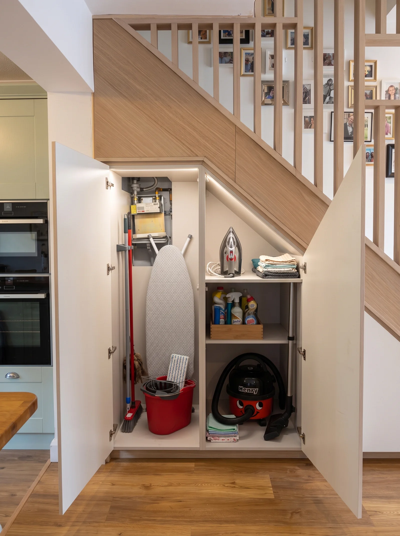 Open understairs cupboard storing a vacuum cleaner, mop and cleaning supplies