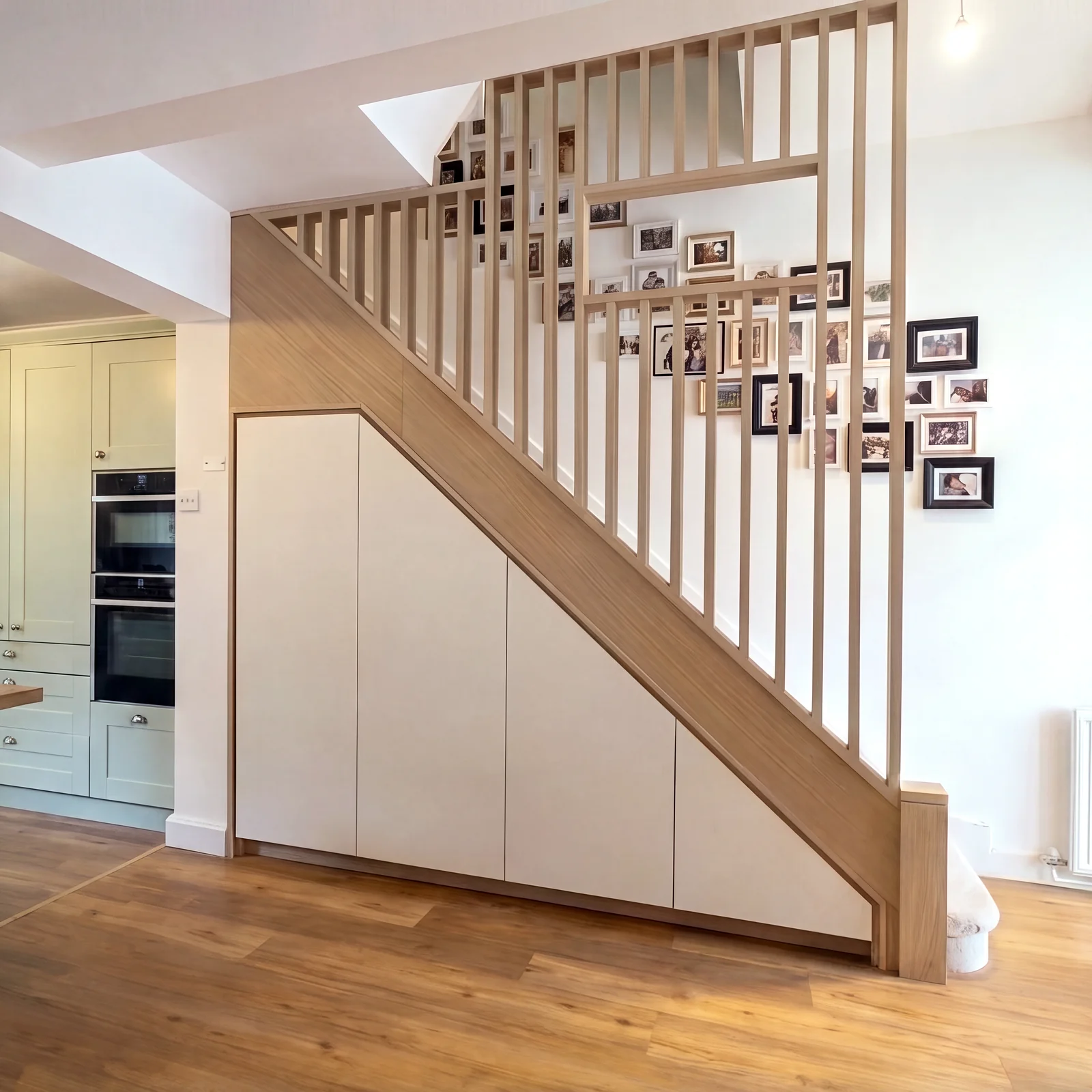 Oak staircase with vertical oak slats and white fitted cupboards below, next to a cream kitchen