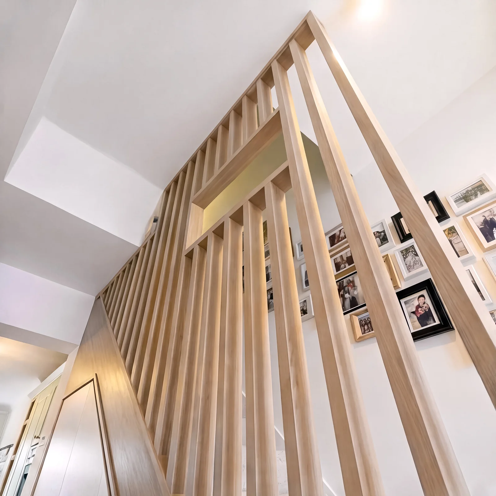 Looking up an oak staircase through a vertical slatted oak screen with family photos