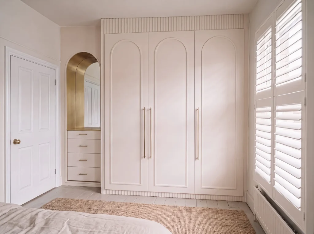 Blush pink fitted wardrobe with arched doors and an arched dressing alcove in Notting Hill