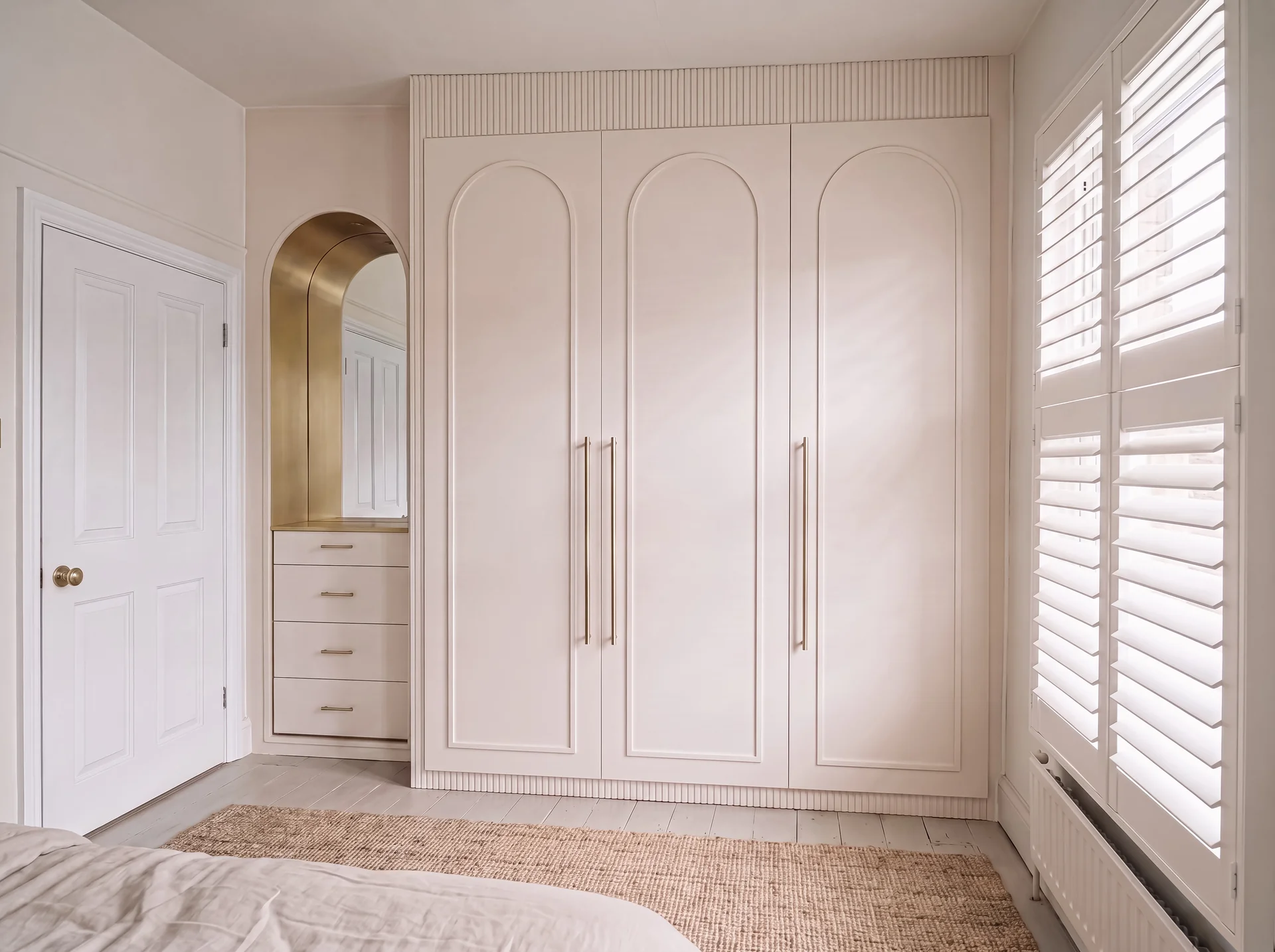 Blush pink fitted wardrobe with arched doors and an arched dressing alcove in Notting Hill