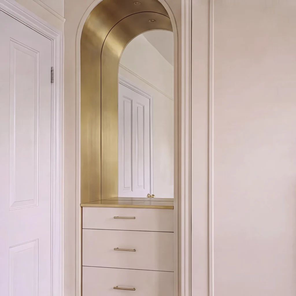 Arched dressing alcove with a brass-lined arch, mirror and blush drawers