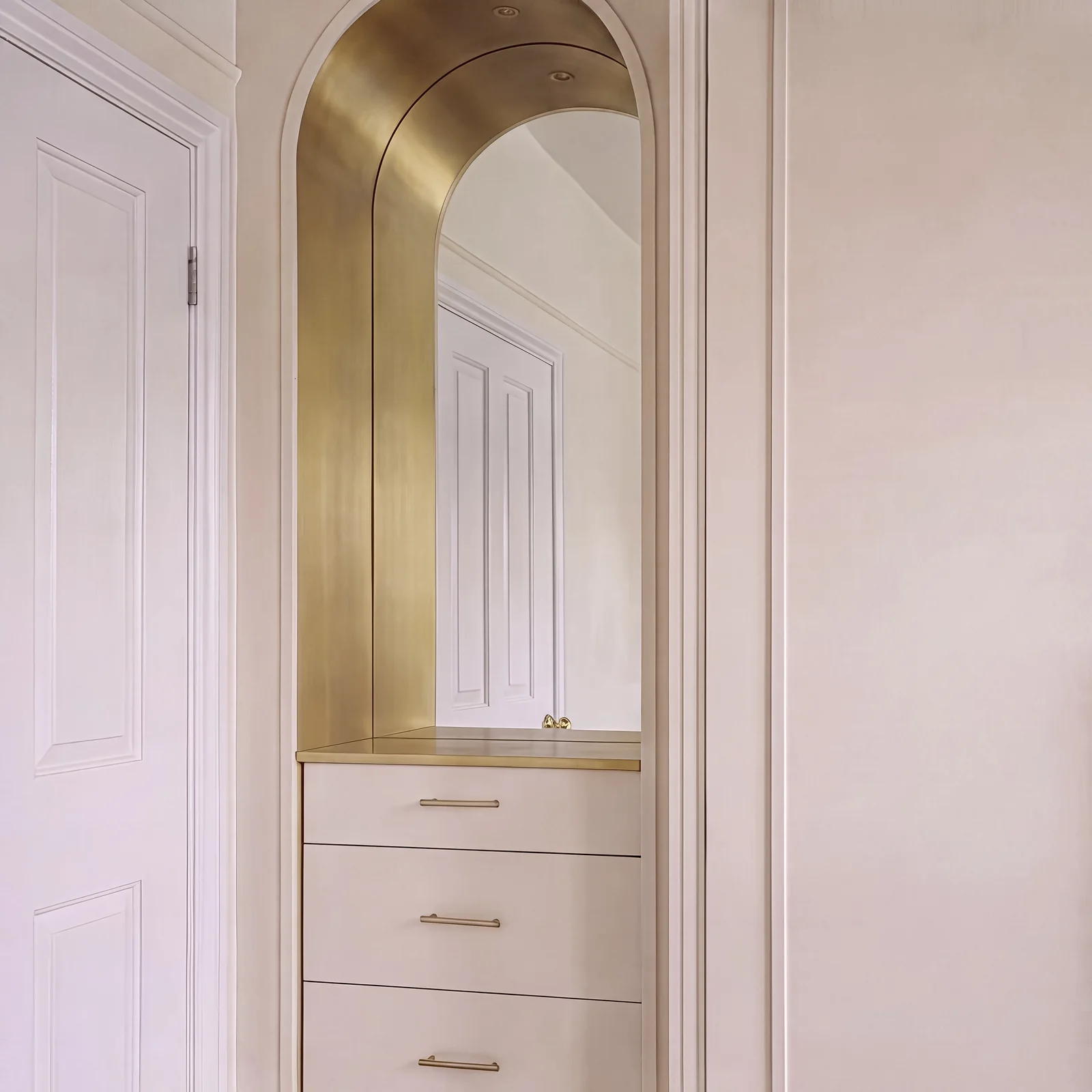 Arched dressing alcove with a brass-lined arch, mirror and blush drawers