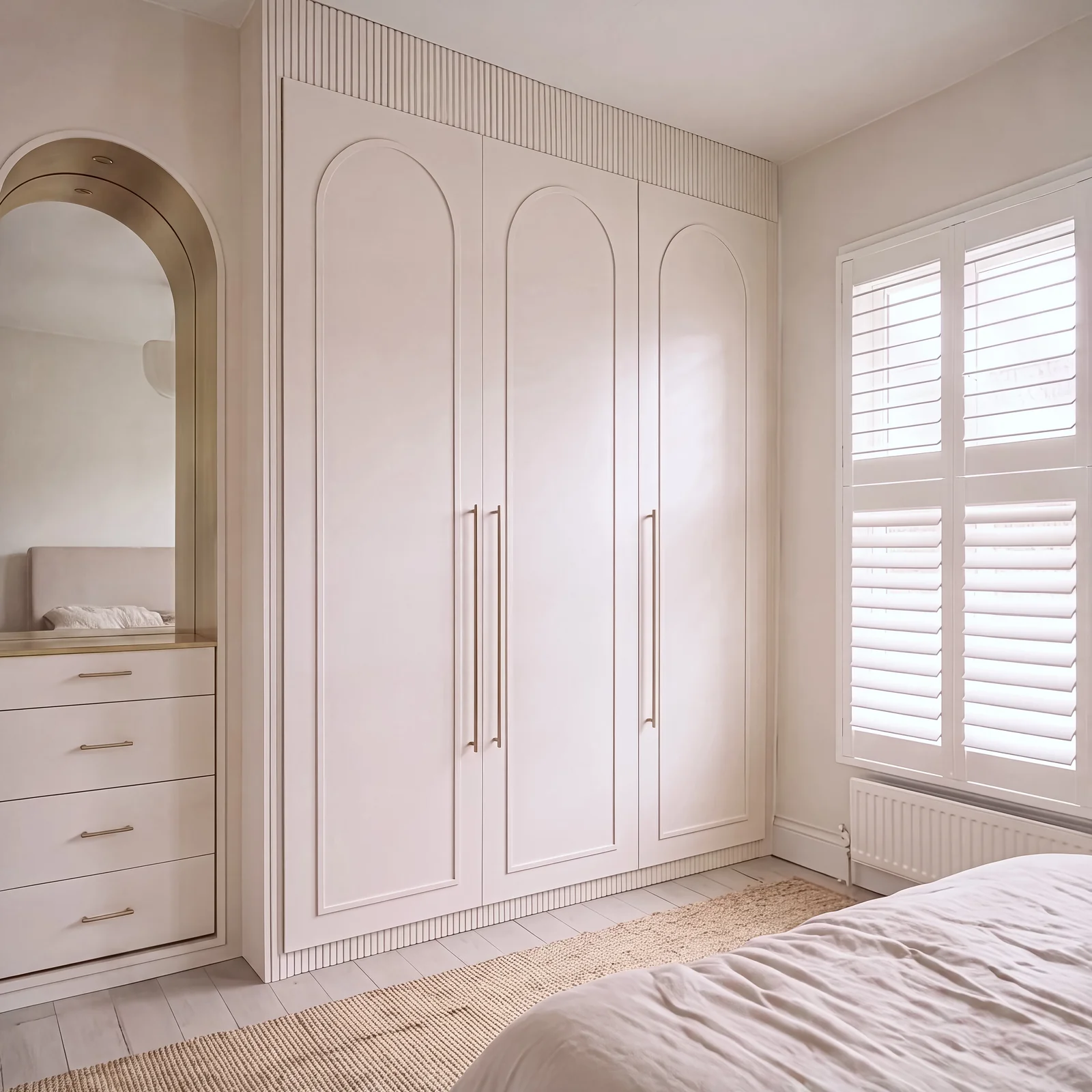 Blush arched wardrobe with a reeded top panel beside an arched mirror alcove and shuttered window