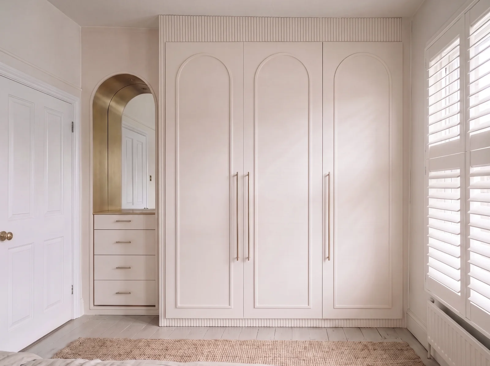 Fitted wardrobe in Notting Hill: closed blush wardrobe with arched door panels and long brass handles in Notting Hill