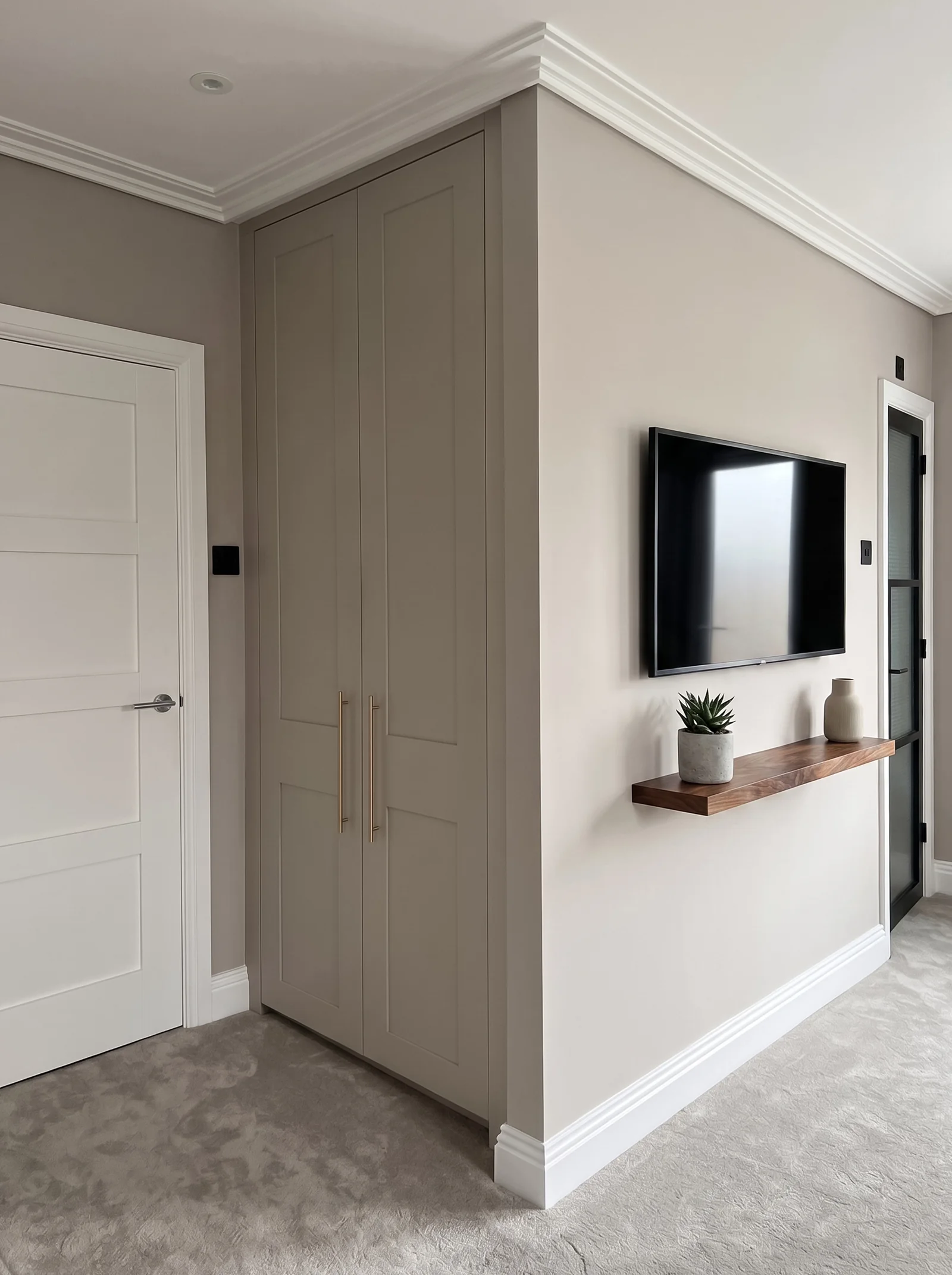 Pale grey wardrobe in a bedroom corner beside a wall-mounted TV and walnut shelf