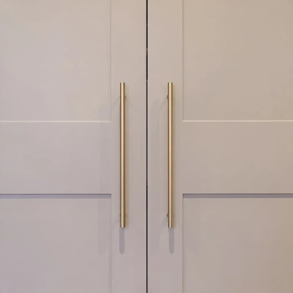 Close-up of brass bar handles on pale grey shaker doors with a horizontal rail