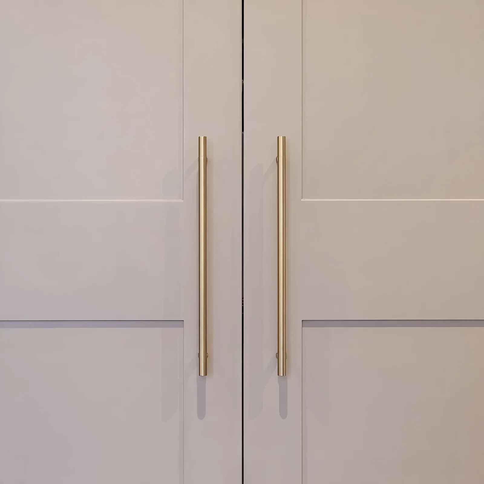 Close-up of brass bar handles on pale grey shaker doors with a horizontal rail