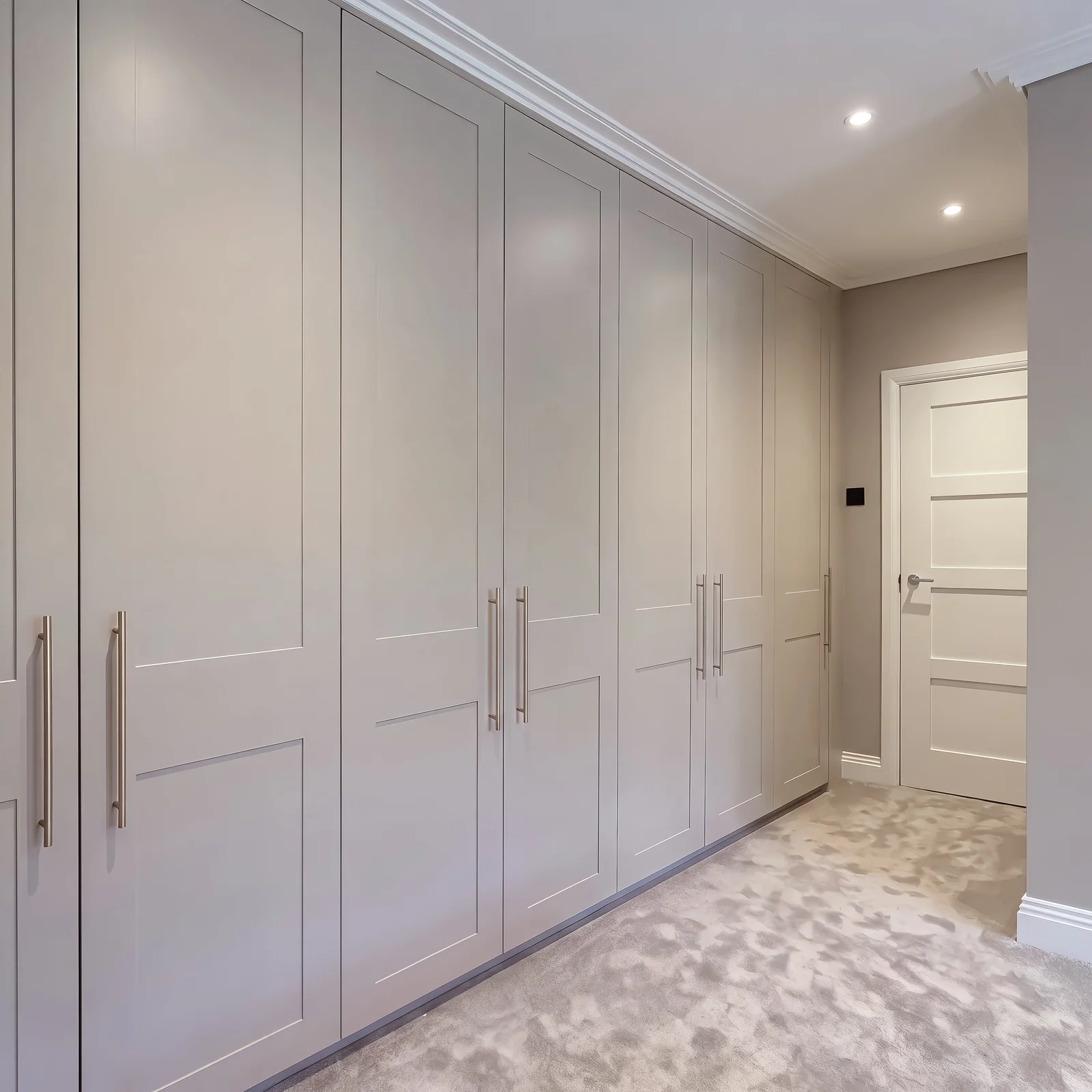 Floor-to-ceiling pale grey shaker wardrobes running along a bedroom wall